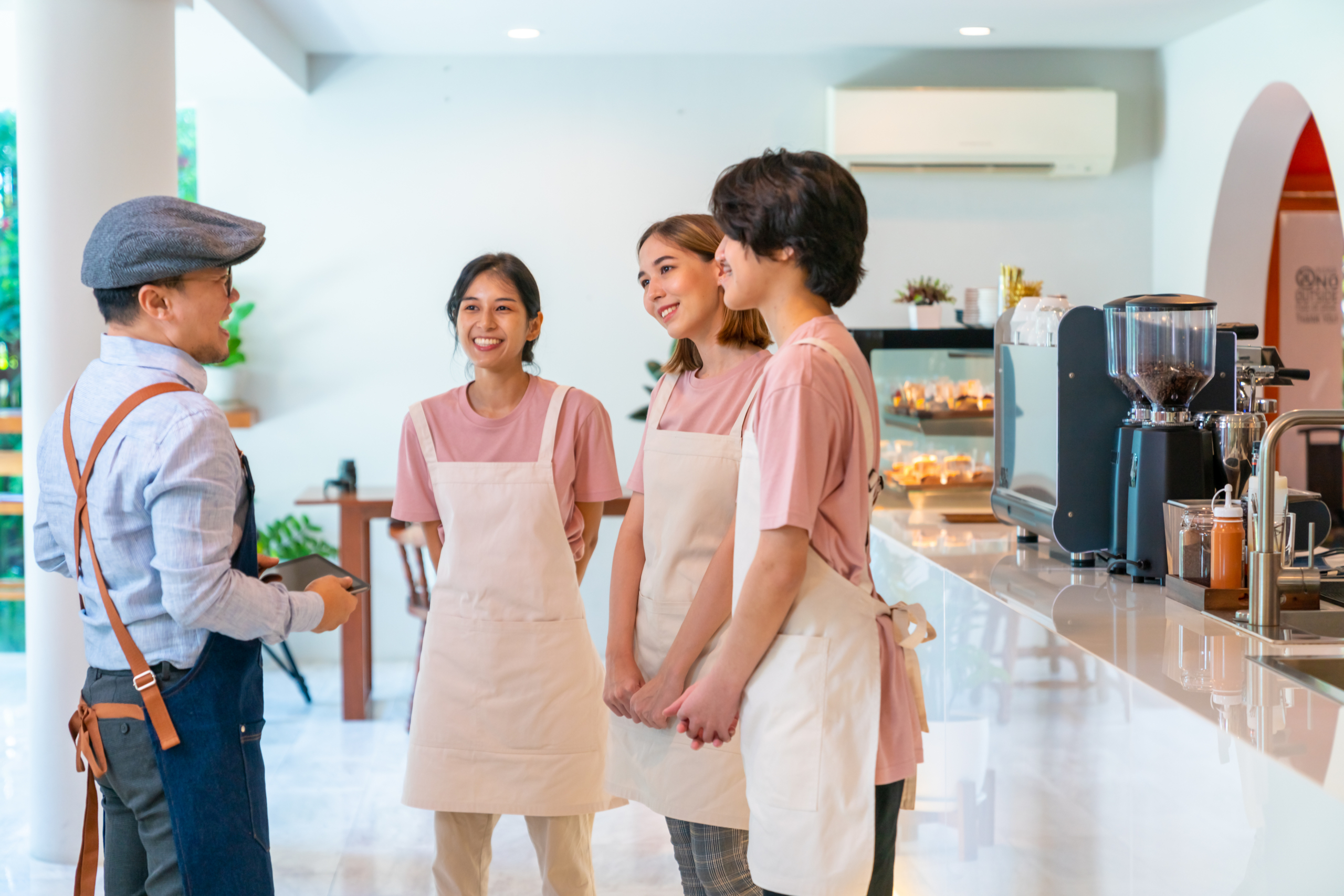 Asian man cafe owner briefing part time employee before opening Asian male coffee shop manager briefing man and woman staff team before working. Small business cafe and restaurant owner instruct part time employee preparing service to customers before opening