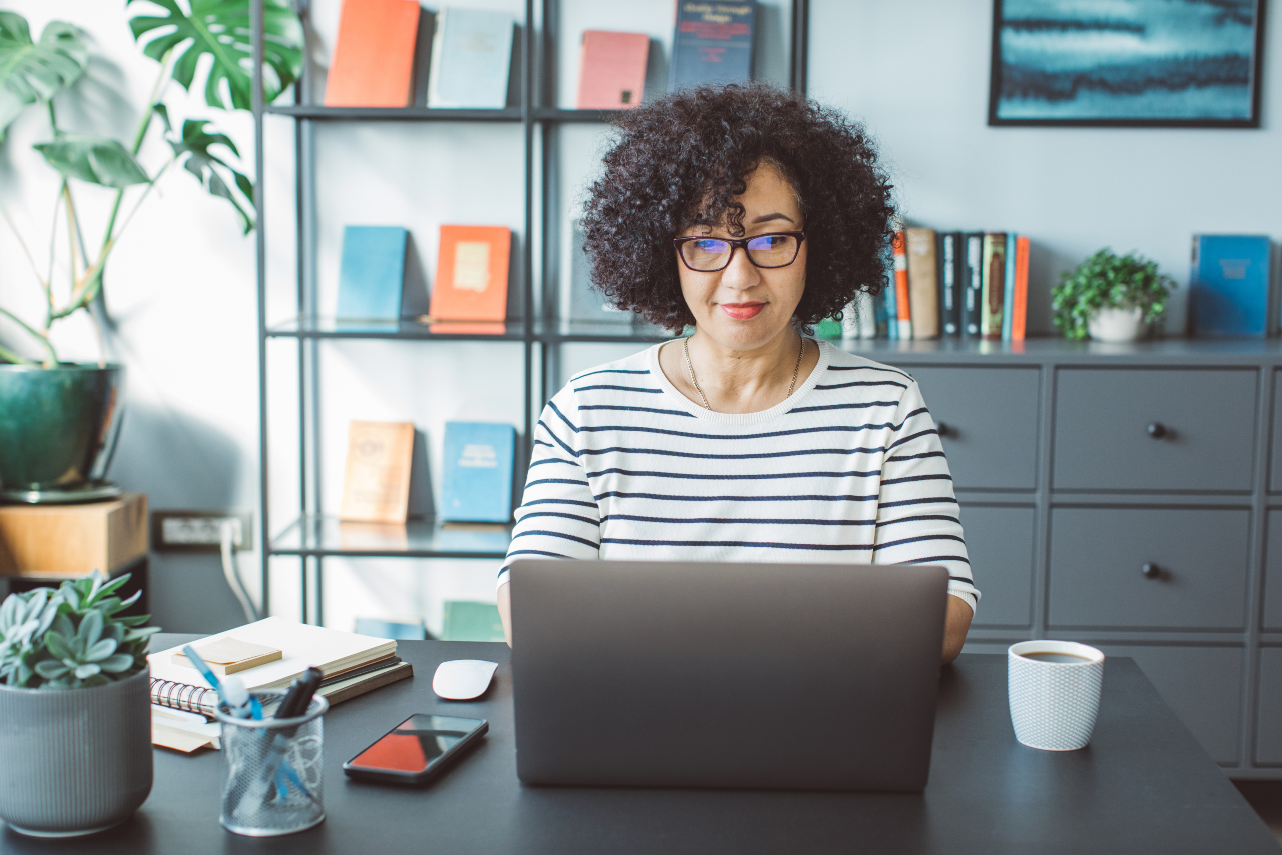 Book publisher at office Mature woman at her office. She is book publisher and reading book script or writing mail on laptop.