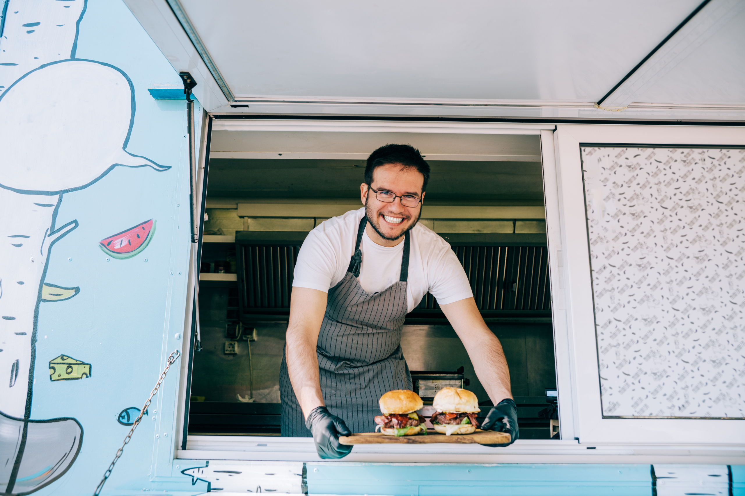 Food truck owner serving burgers. Shot of young smiling chef serving tasty burgers from the window of his food van.